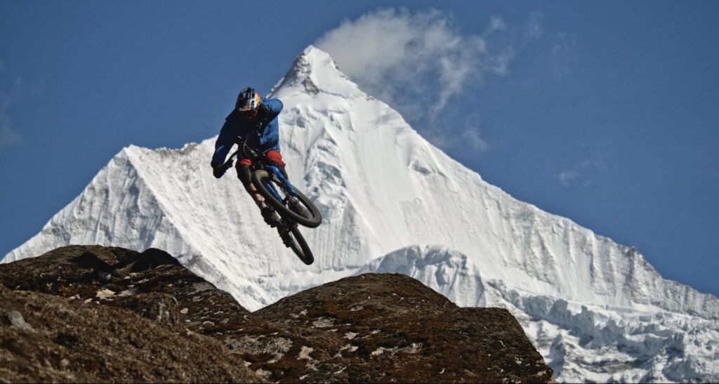 A rider launches off a ridge above snow peaks