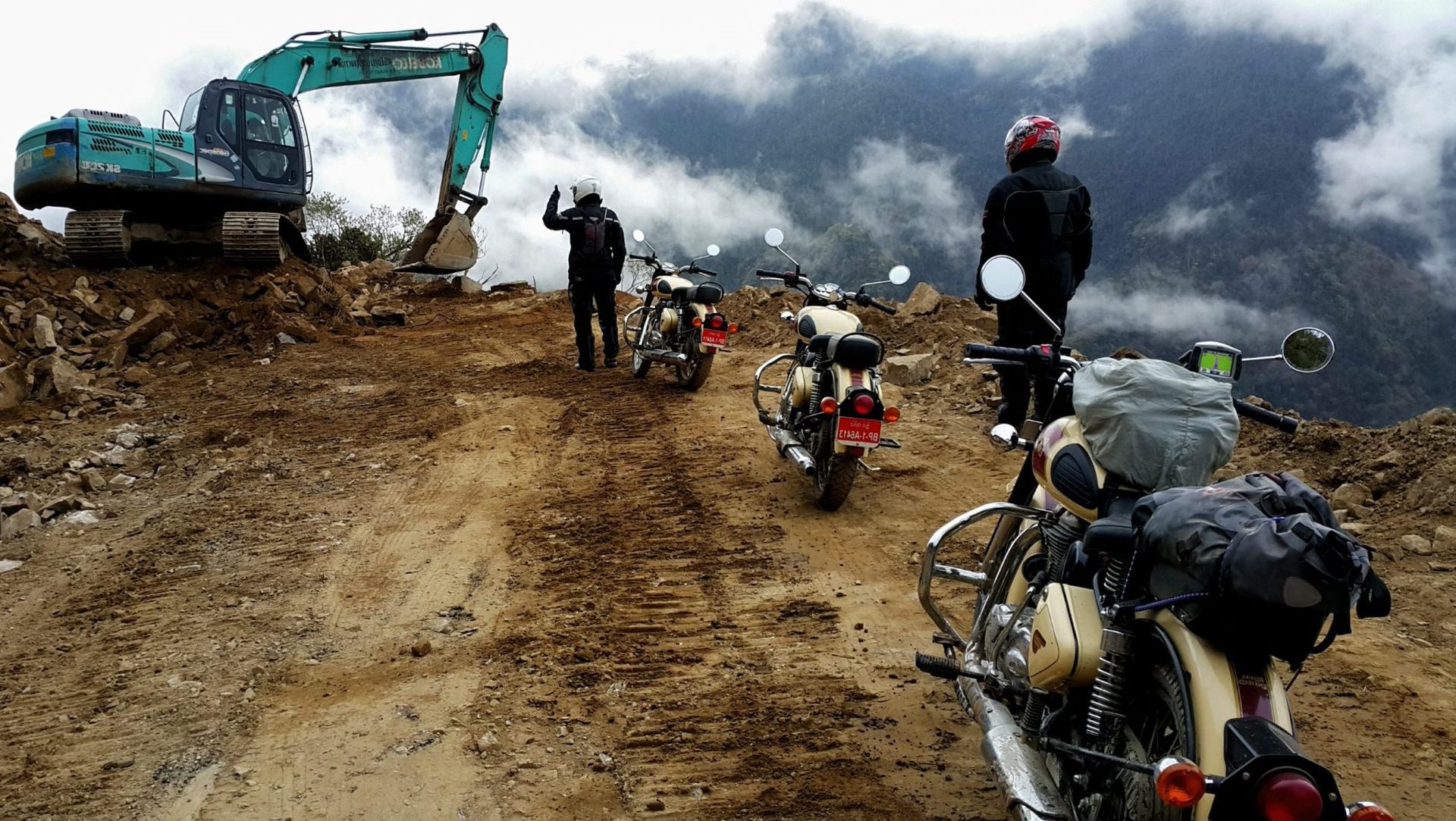A convoy of Royal Enfield motorcycles pauses on a high prayer-flag pass